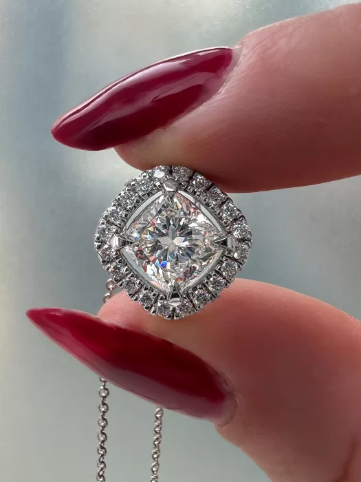 Platinum Cushion Cut Diamond with Diamond Halo Pendant Held in Between Two Fingers