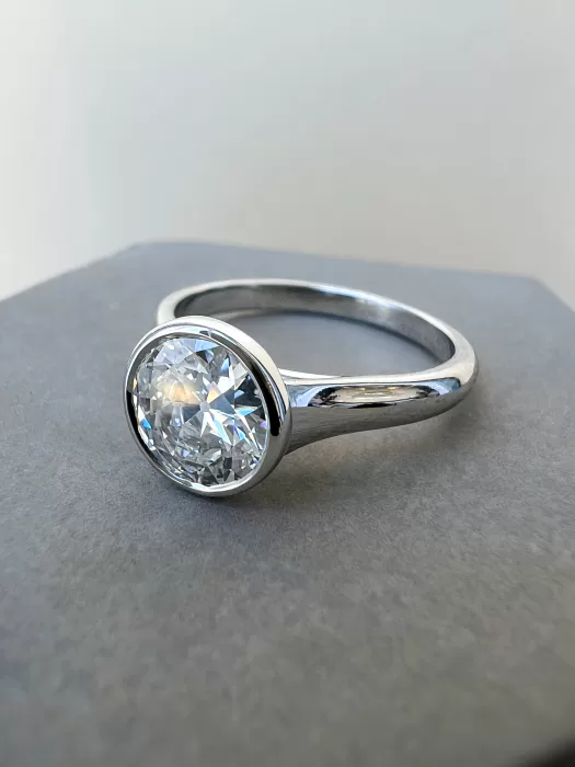 A close-up photograph of a round brilliant diamond solitaire engagement ring with a modern bezel setting, handcrafted in platinum by W&W Jewellery.