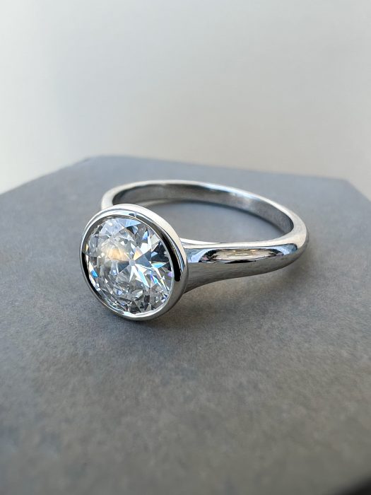 A close-up photograph of a round brilliant diamond solitaire engagement ring with a modern bezel setting, handcrafted in platinum by W&W Jewellery.