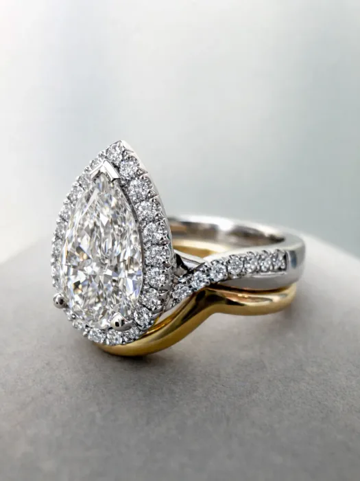 Custom Pear Cut Diamond Halo Engagement Ring on concrete table with wedding ring