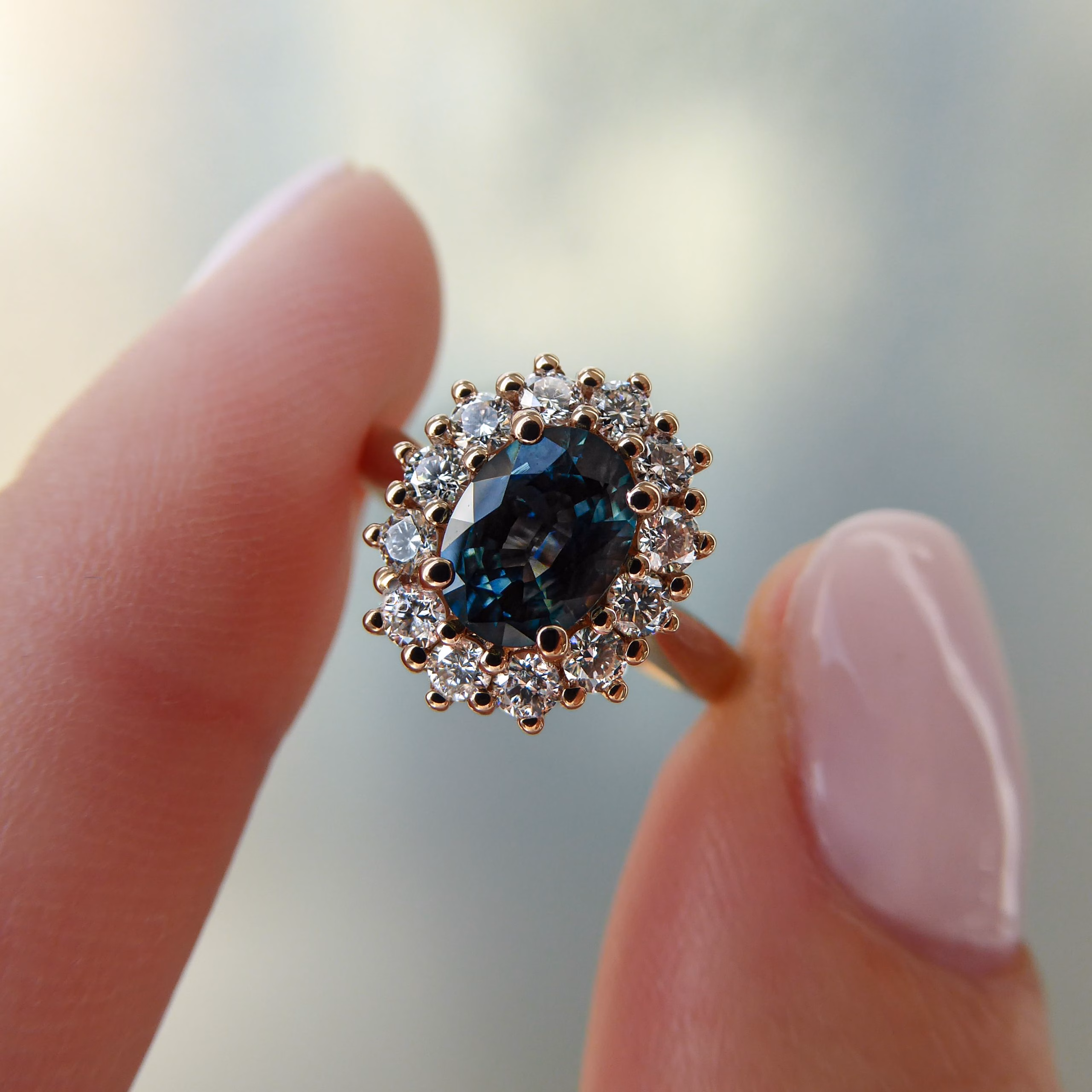 Ring Fingers teal sapphire vintage bespoke engagement ring being held between finger and thumb