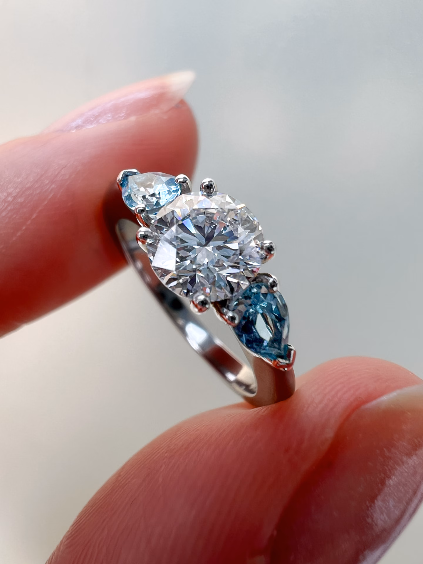 Diamond and Aquamarine Three Stone Engagement Ring Diamond and Aquamarine Three Stone Engagement Ring between fingers